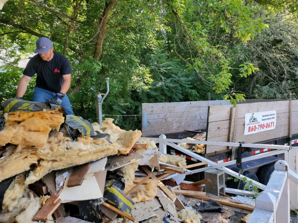 Man loading a pile of insulation and debris into a large open trailer with wood sides
